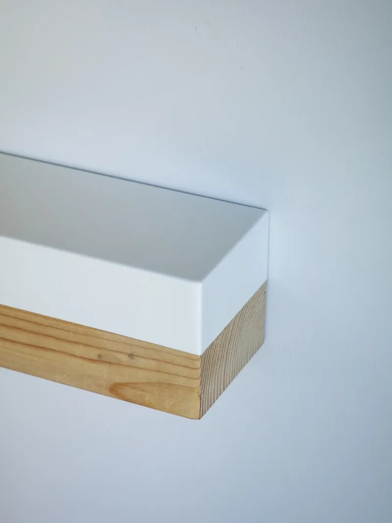 Corner detail of a white painted shelf with exposed timber edge against a pale wall