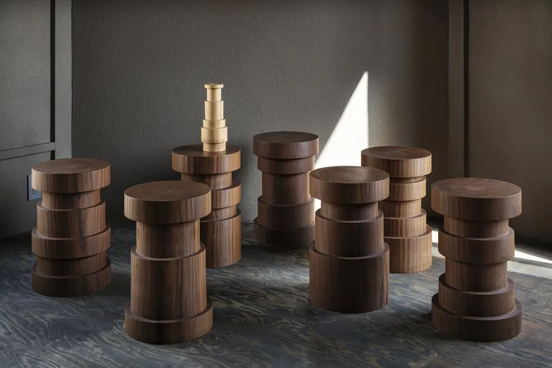 Group of stacked cylindrical timber stools on a patterned floor in afternoon light