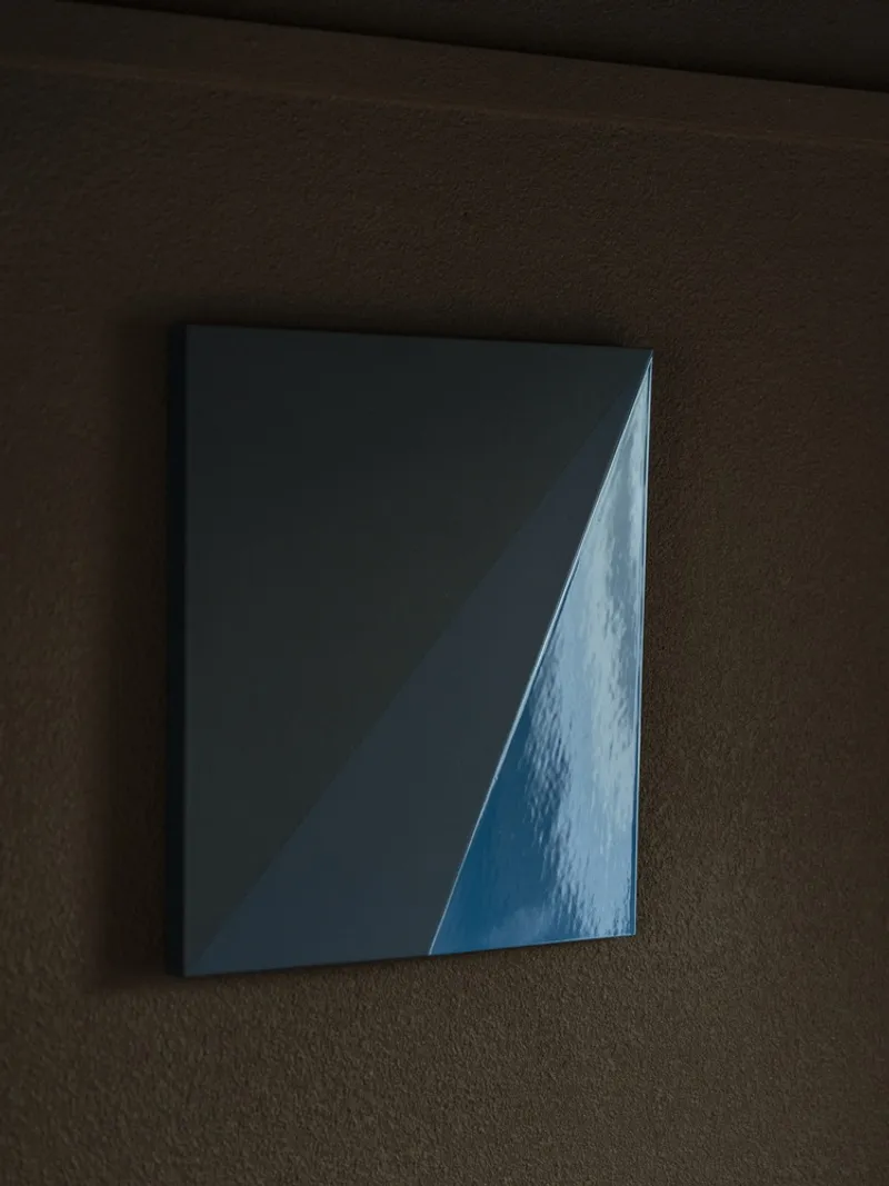 Blue glazed ceramic tile mounted on a textured brown wall in dim lighting