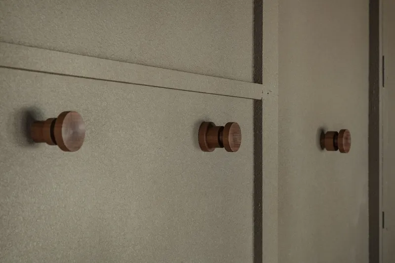 Three turned timber wall hooks mounted on a pale textured wall with vertical paneling