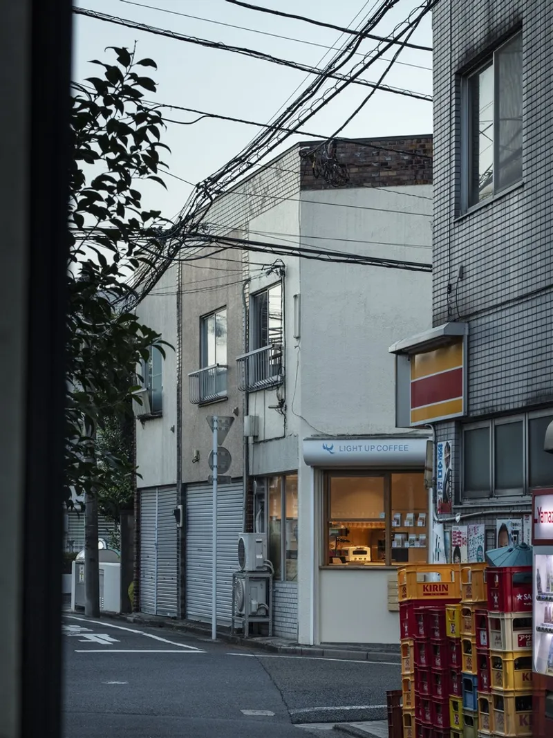 Street view of narrow mixed-use buildings with overhead power lines and stacked beverage crates at dusk