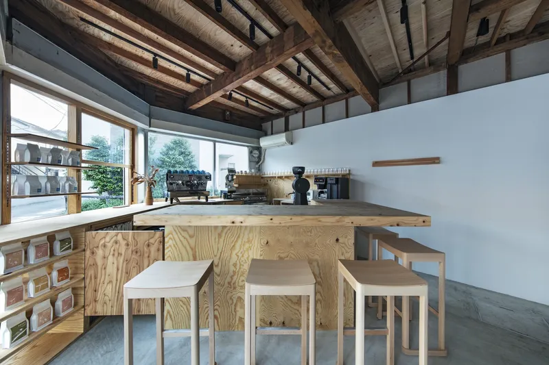 Coffee bar with plywood counter and espresso machines beneath exposed timber beams and clerestory windows