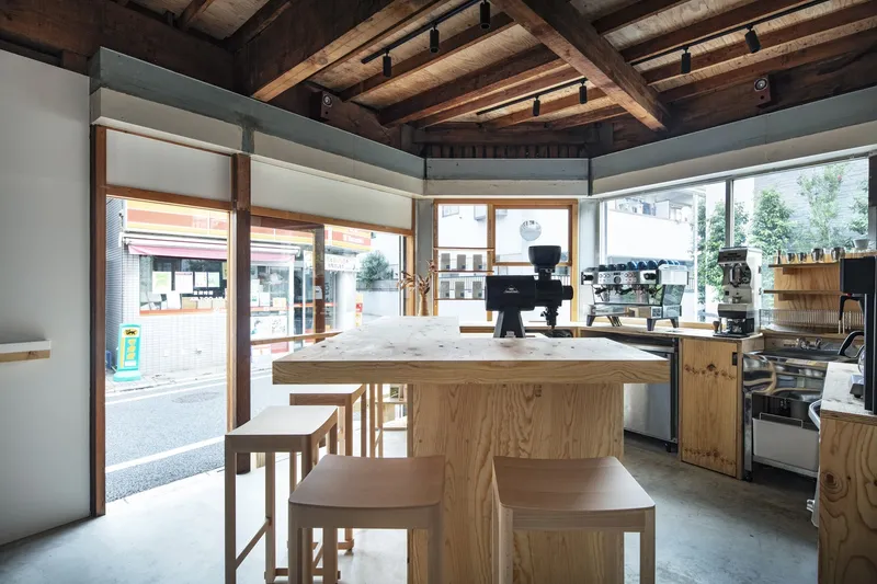 View from plywood service counter toward street-facing windows with timber frames and roller shades