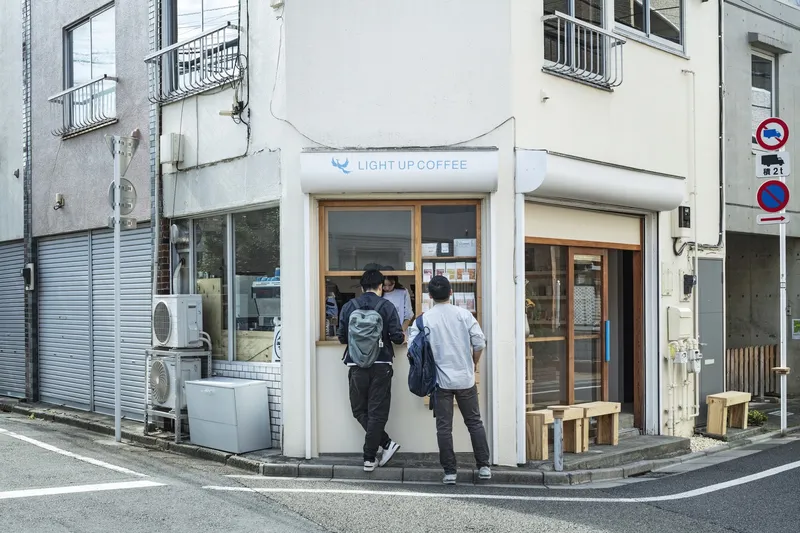 Corner entrance with two customers approaching the curved white facade and timber-framed doorway