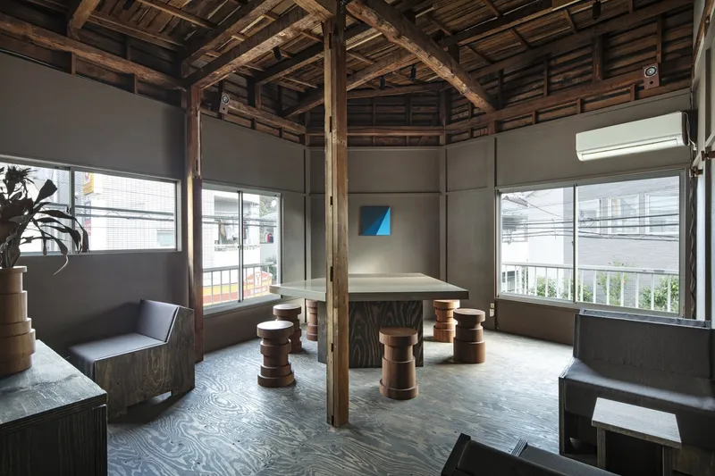 Interior space with exposed timber frame structure, grey plywood walls and cylindrical wooden stools around a central table