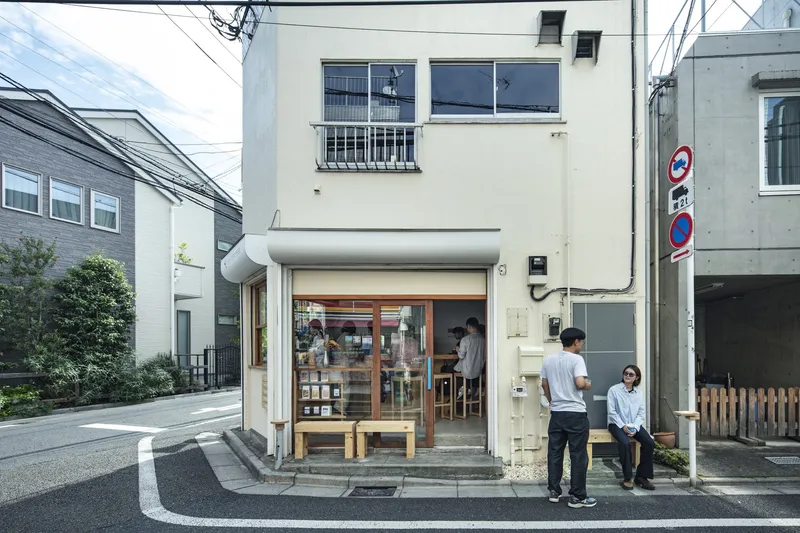 Street view of the white shopfront with open glazed doors and two pedestrians on the sidewalk