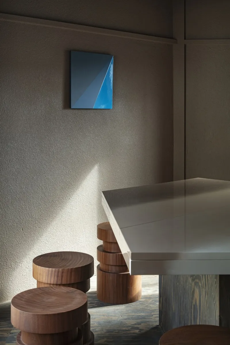 Corner seating area with layered timber stools catching afternoon sunlight beneath blue geometric artwork