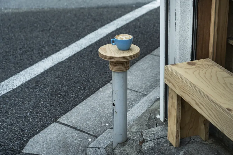 Outdoor side table fashioned from repurposed steel post with plywood top holding coffee cup