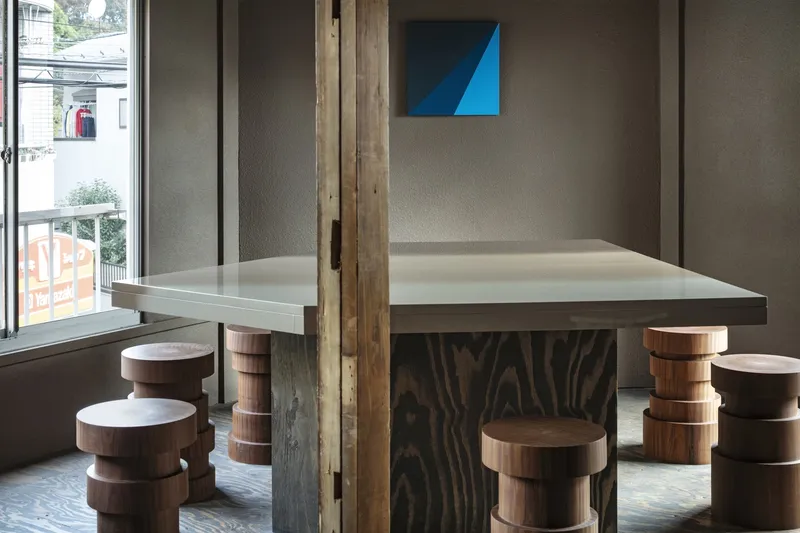 Custom communal table with thick plywood base and circular timber stools beside glazed storefront
