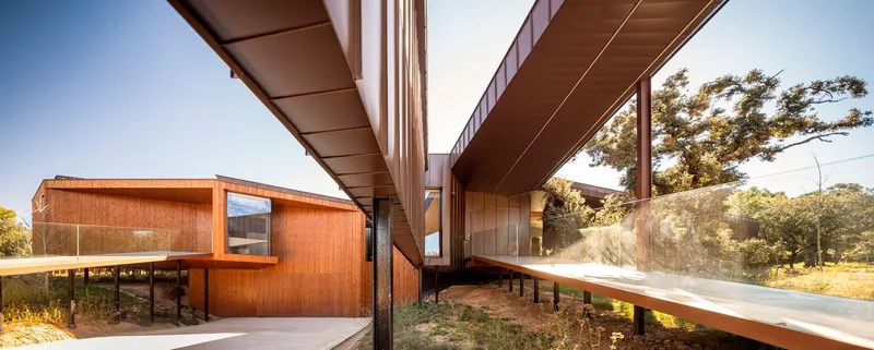 Covered walkway beneath intersecting roof planes supported by slender steel columns in afternoon sun