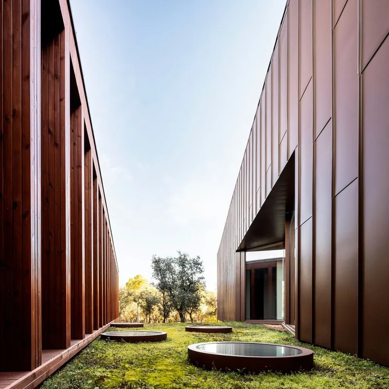Courtyard view between vertical timber screen wall and metal panel facade with circular reflecting pools