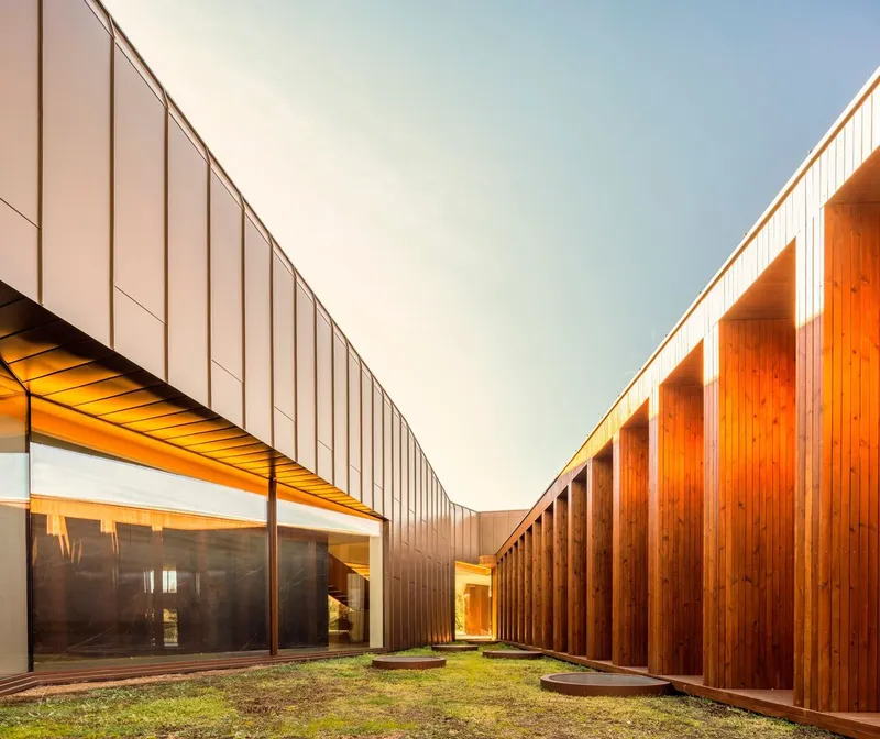 Courtyard junction where vertical timber slat walls meet metal panel facades with grass and lighting at twilight