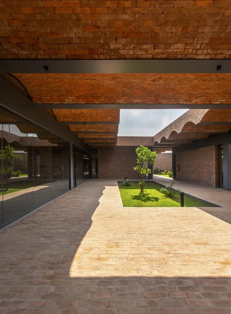 Brick pathway beneath undulating vaulted canopy with central lawn and planted trees