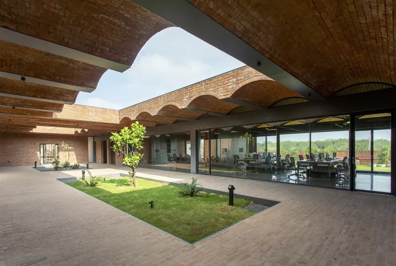 Interior courtyard with brick paving and central lawn bed beneath undulating brick vault ceilings