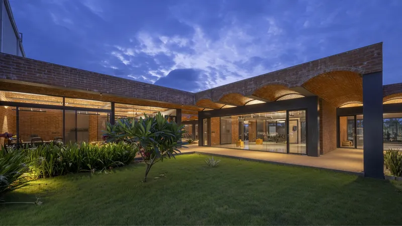 Courtyard view at dusk with illuminated glazed walls and grass lawn surrounded by planted beds