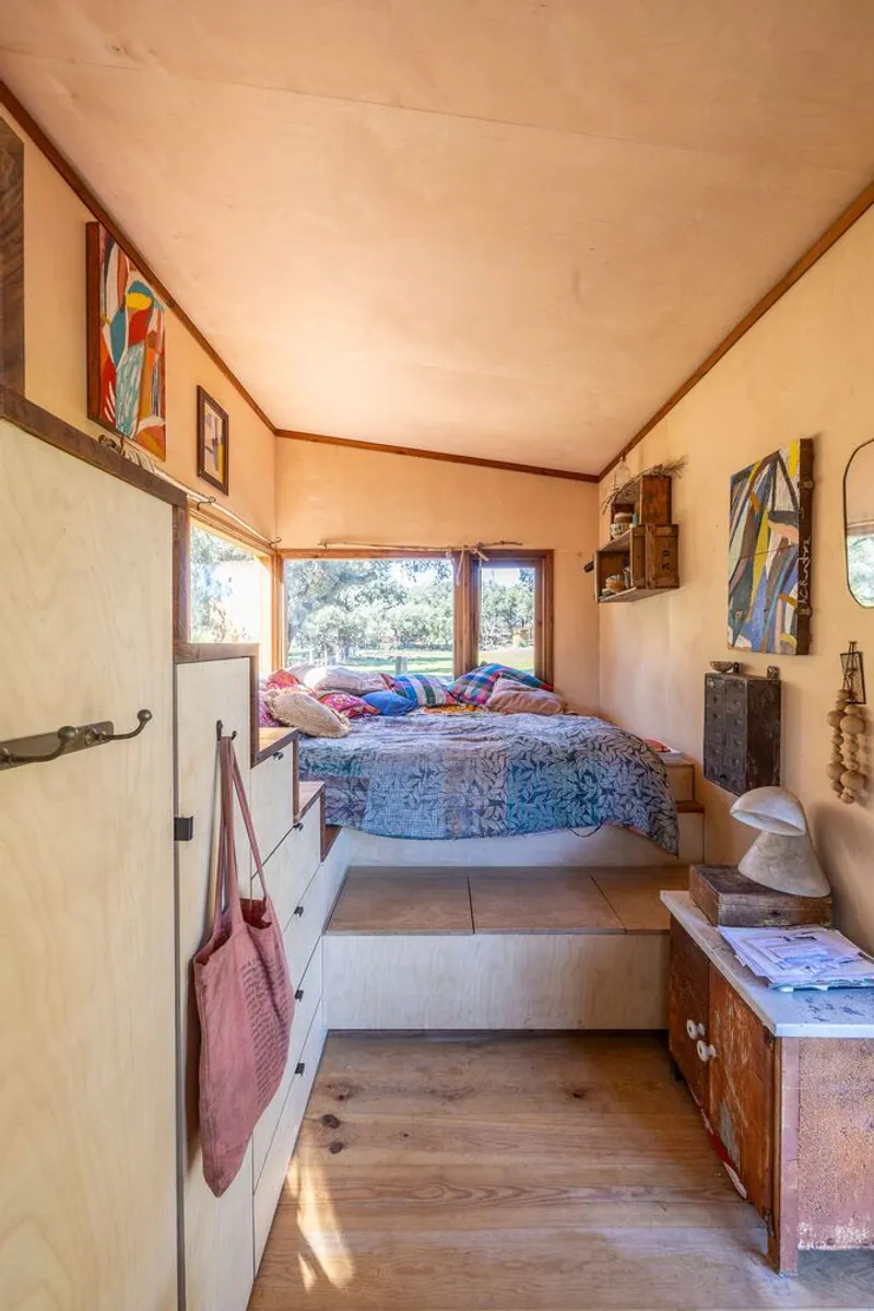 Compact sleeping alcove with raised platform bed beneath plywood ceiling and horizontal windows