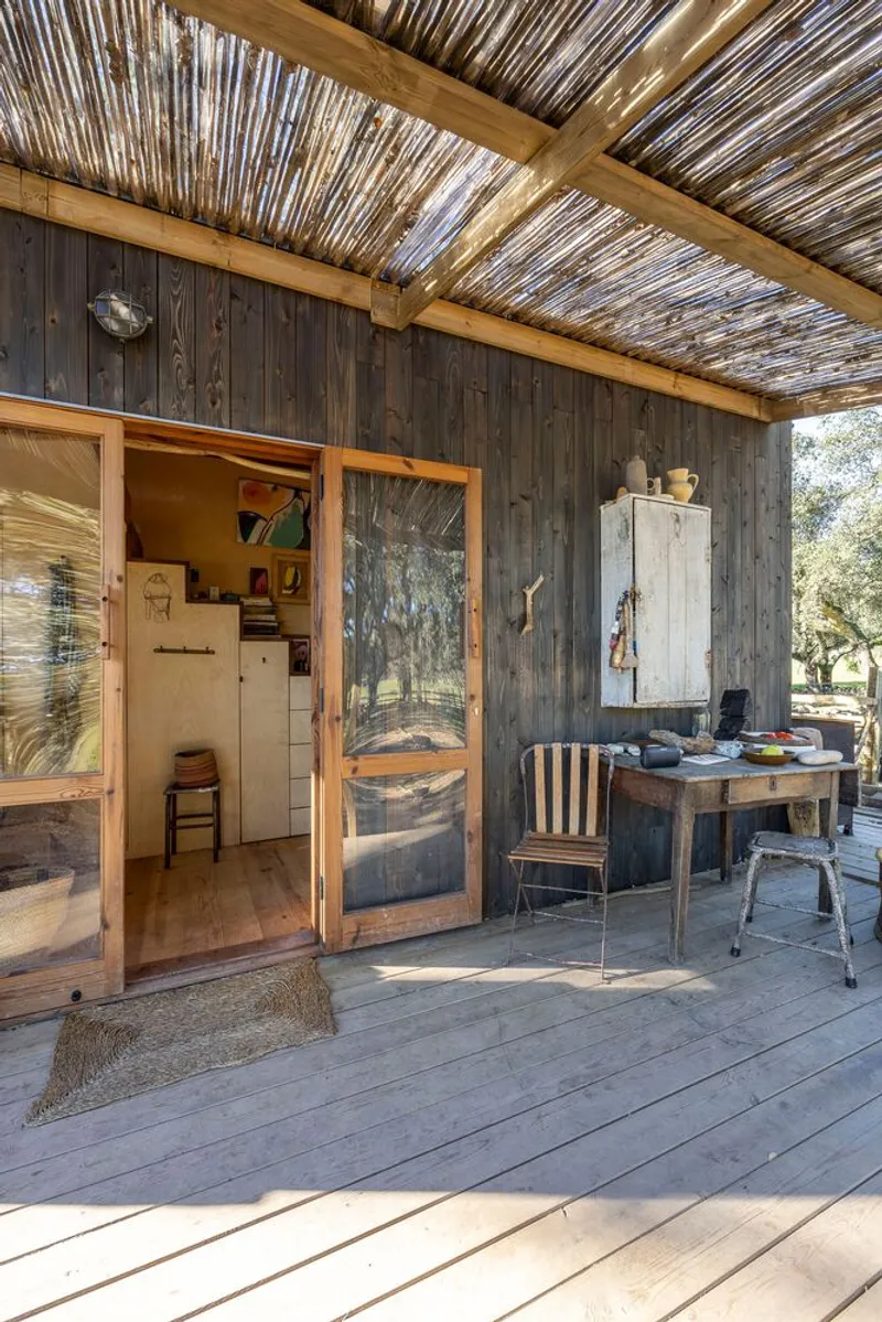 Covered deck with slatted reed ceiling and sliding glass doors opening to plywood interior