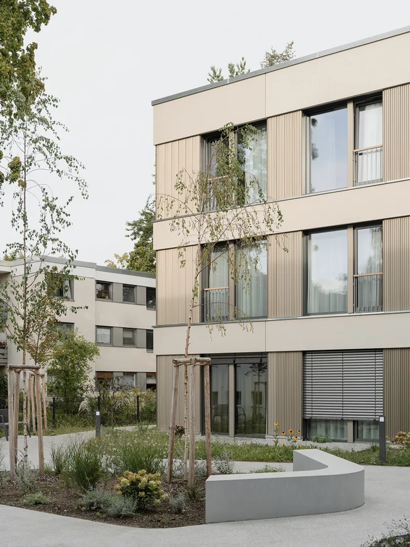 Corner view of vertical ribbed cladding panels with inset balconies and a curved concrete planter below