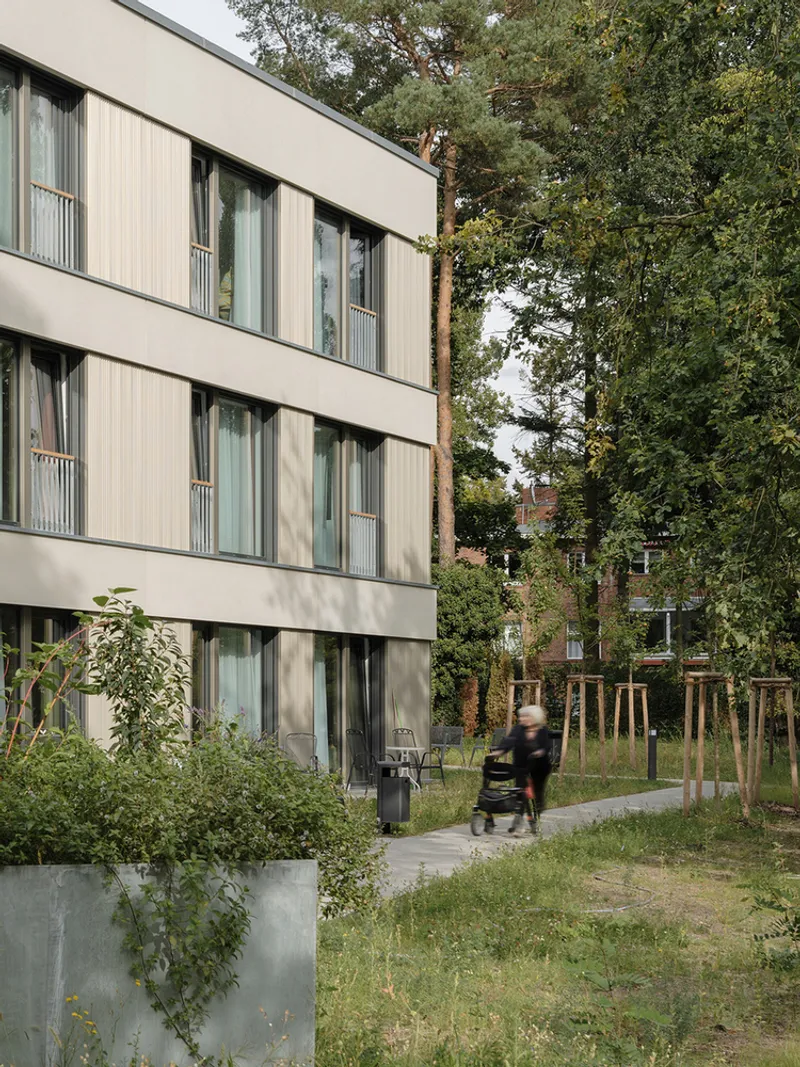 Ground-floor facade with ribbed panels and a person with a stroller passing along the pathway