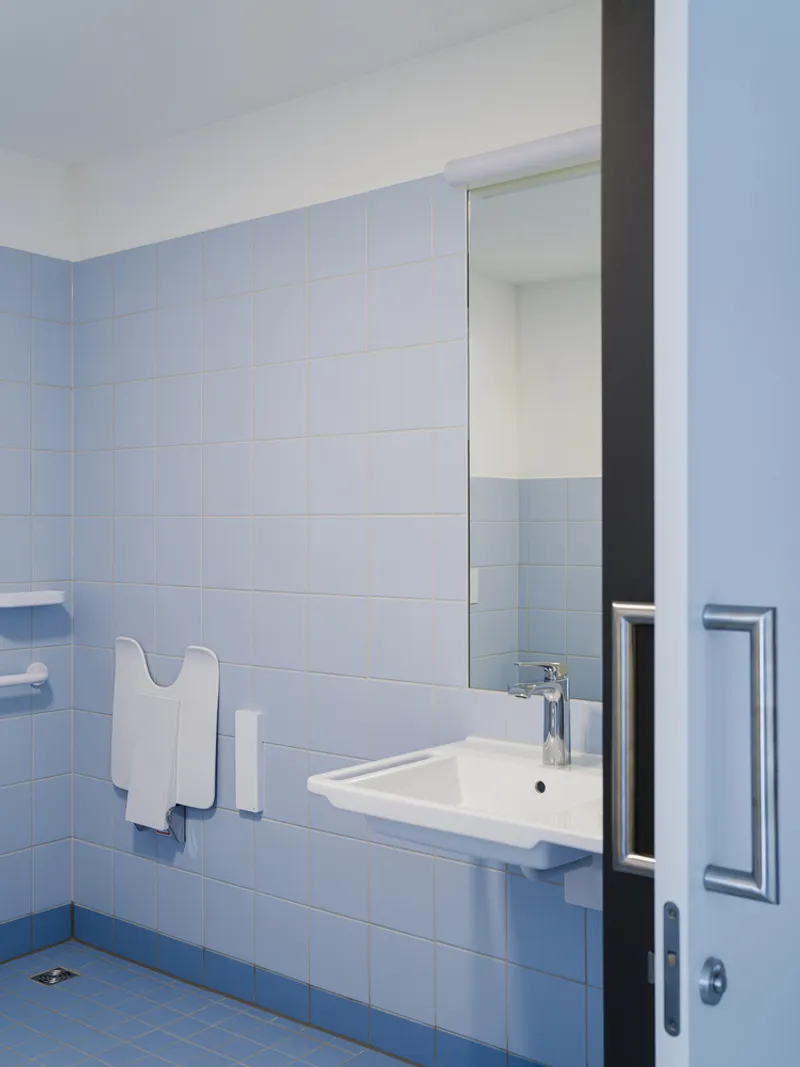 Bathroom detail showing light blue square tile wall with wall-hung sink and dark-framed sliding door