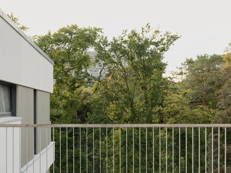 White balcony railing with vertical metal bars facing mature deciduous trees under an overcast sky