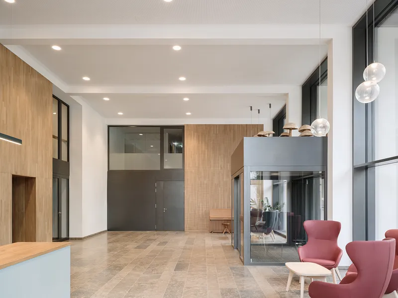 Double-height lobby with oak-clad walls, glass pendant lights and pink upholstered chairs