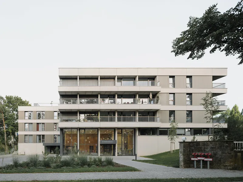 Street view of the residential building with stacked balconies and ground-floor glazing framed by trees