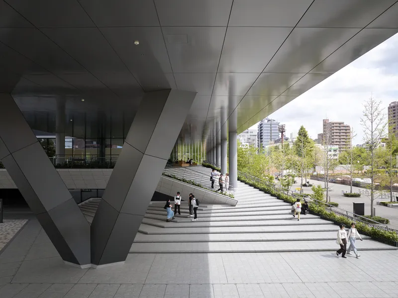 Wide staircase ascending beneath an angular cantilevered overhang clad in faceted metal panels