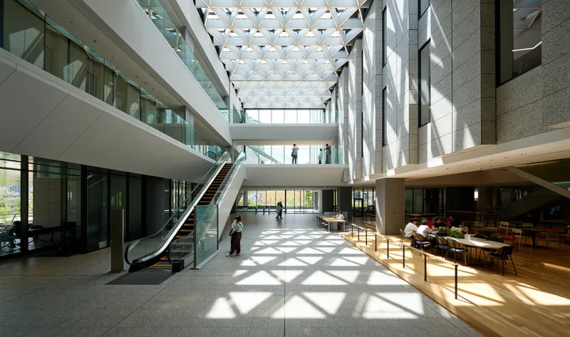 Multi-story atrium with a triangular patterned skylight casting geometric shadows across the timber floor