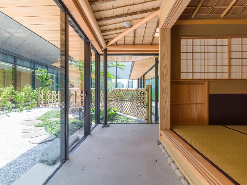 Covered timber corridor opening to a courtyard garden with folding glass doors and tatami room beyond