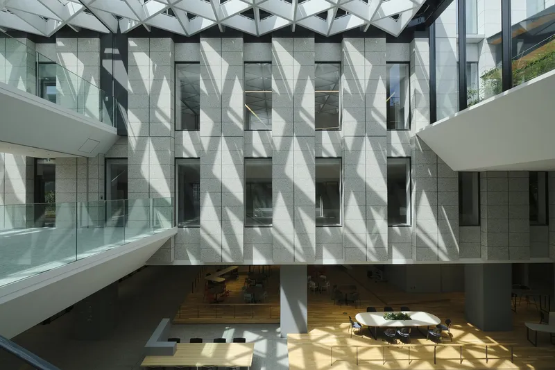 Interior courtyard with faceted concrete facade and geometric glazed skylight casting shadows over a timber-floored atrium