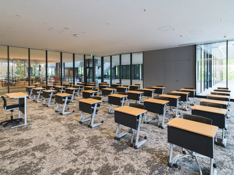 Classroom with rows of individual desks facing a grey wall panel and floor-to-ceiling glazing