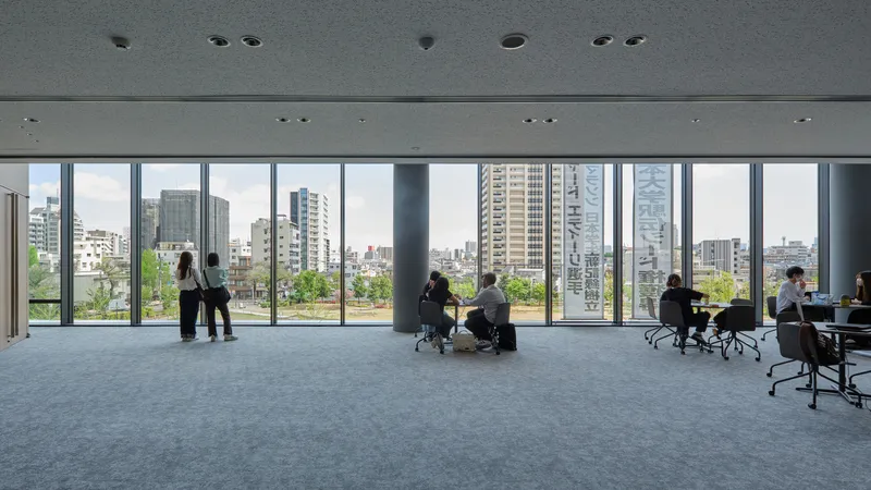 Open office floor with full-height glazing overlooking treetops and residential towers in the distance