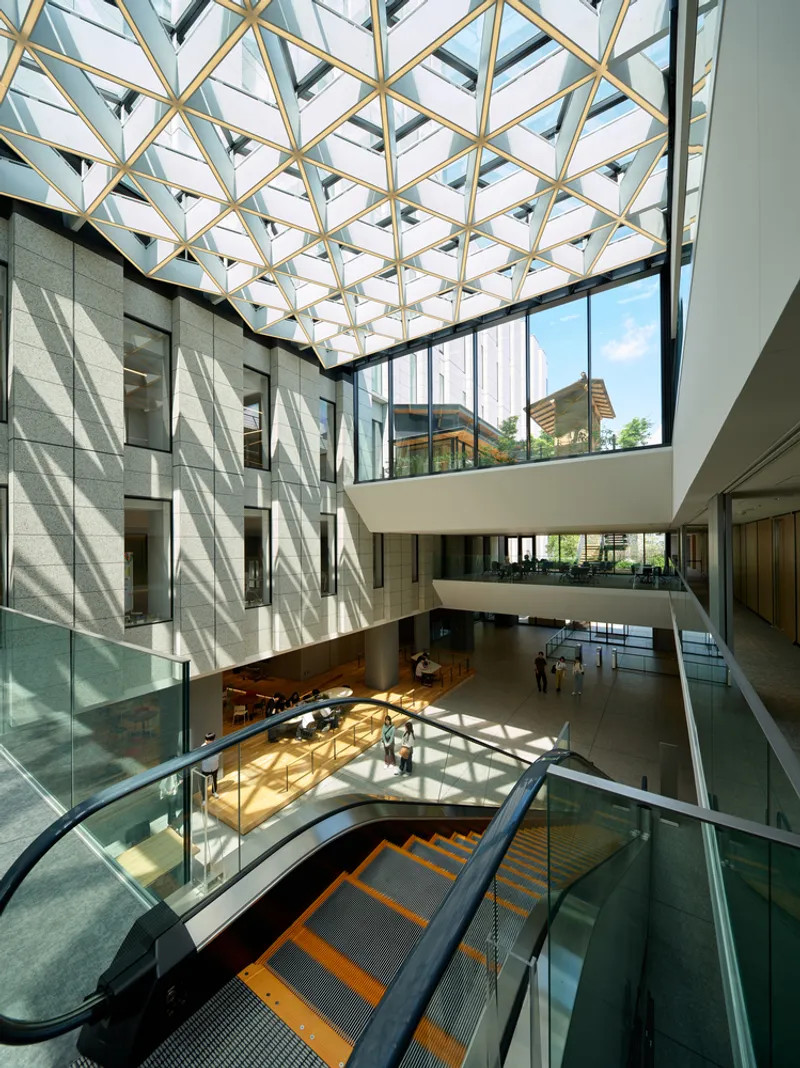Multi-level atrium with escalator, glass balustrades and diamond-pattern skylight filtering afternoon light through the space