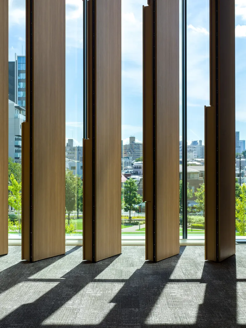 Series of vertical timber louvres framing a view to parkland and distant towers under a partly cloudy sky