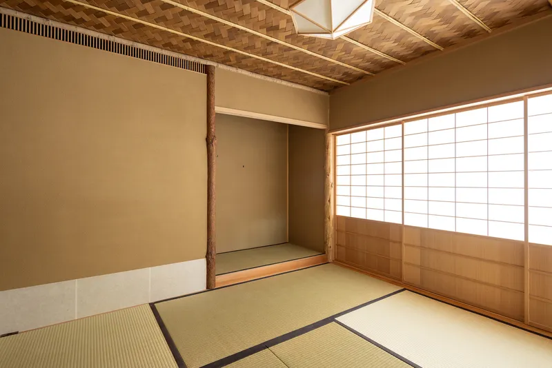 Tatami room with shoji screens, alcove recess, and woven timber ceiling in natural light
