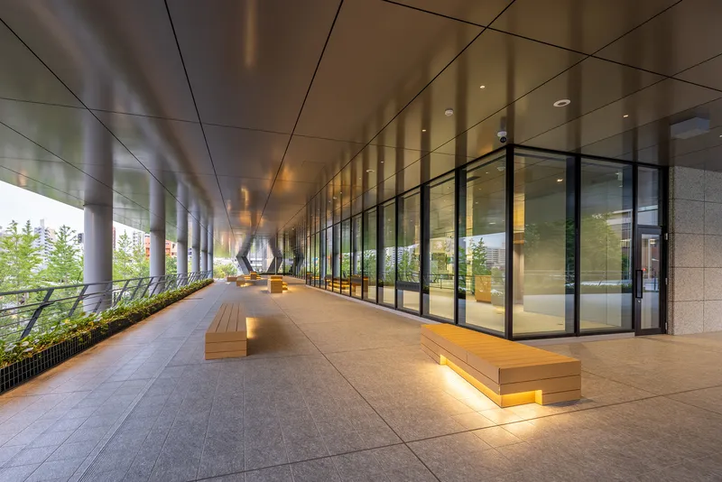 Colonnade corridor with reflective metal ceiling panels and illuminated timber benches at dusk