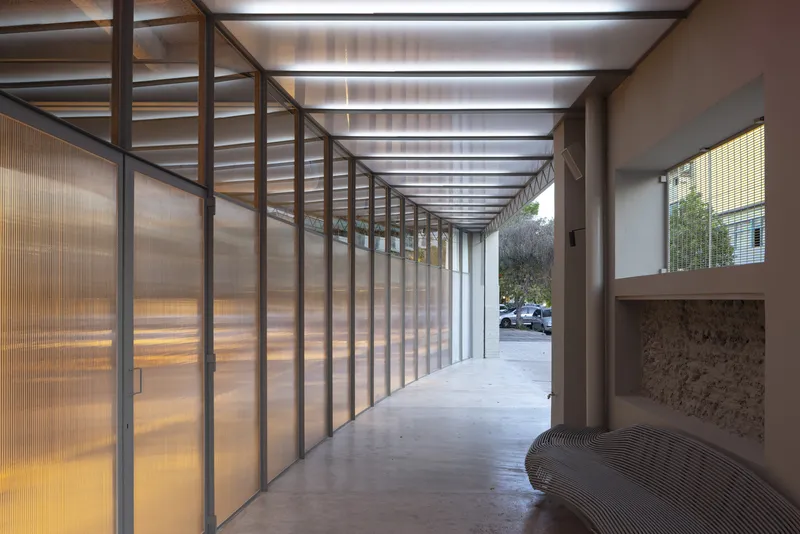Covered entrance passage with ribbed polycarbonate panels and exposed ceiling beams framing the street beyond