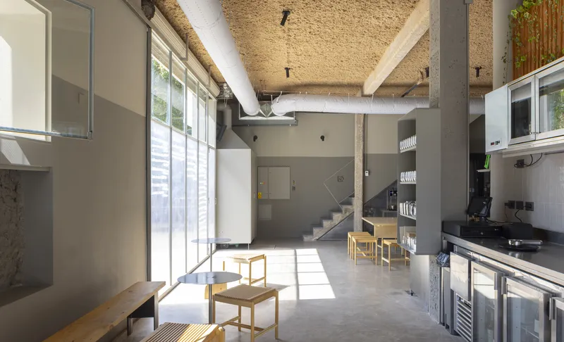 Double-height interior with hempcrete ceiling, exposed ductwork, concrete floor and sunlight streaming through glazing