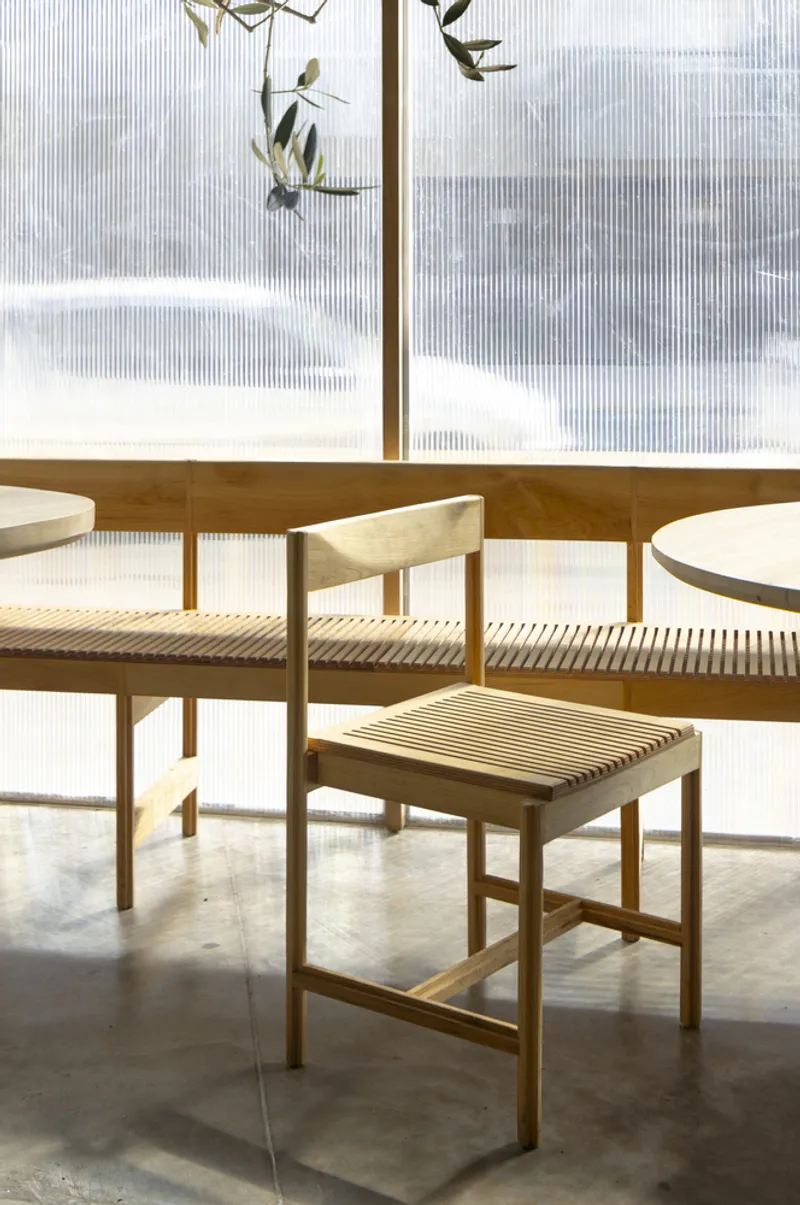 Timber chairs with slatted seats arranged around a table beside fluted glass windows overlooking winter landscape