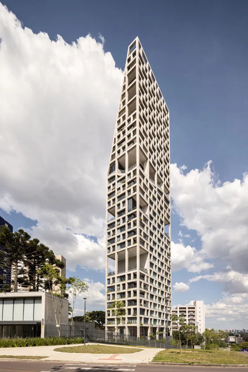 Ground-level view of the tapered tower base with planted beds on a grassy plaza