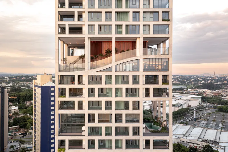 Facade detail showing the double-height communal terrace with timber screens at dusk over the cityscape