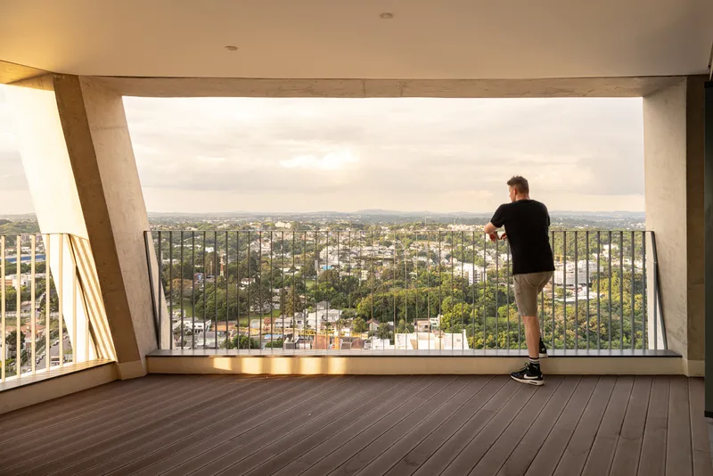 Upper-level terrace with timber decking and angled concrete frame opening to a panoramic view at dusk