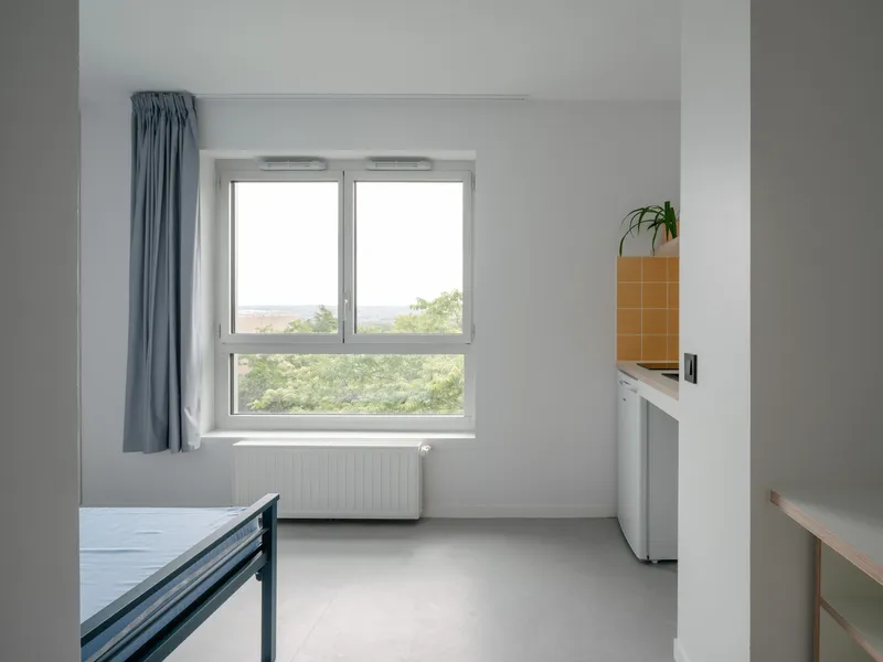 Compact residential room with window overlooking greenery, blue curtain and orange tiled kitchenette