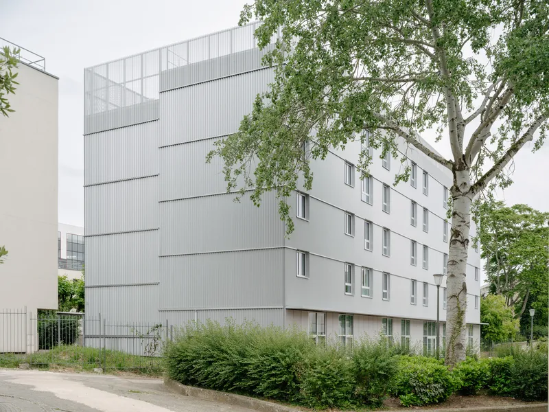 Corner view of the white corrugated metal facade with horizontal fins beside a birch tree