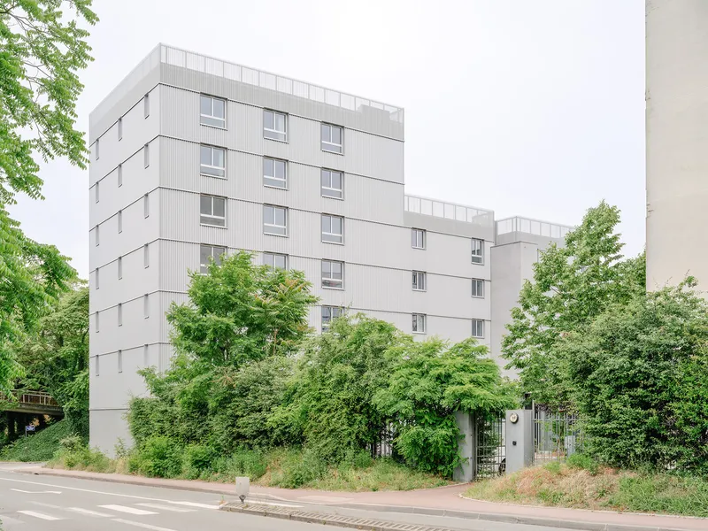 Street view of the five-story housing block with offset volumes surrounded by overgrown vegetation