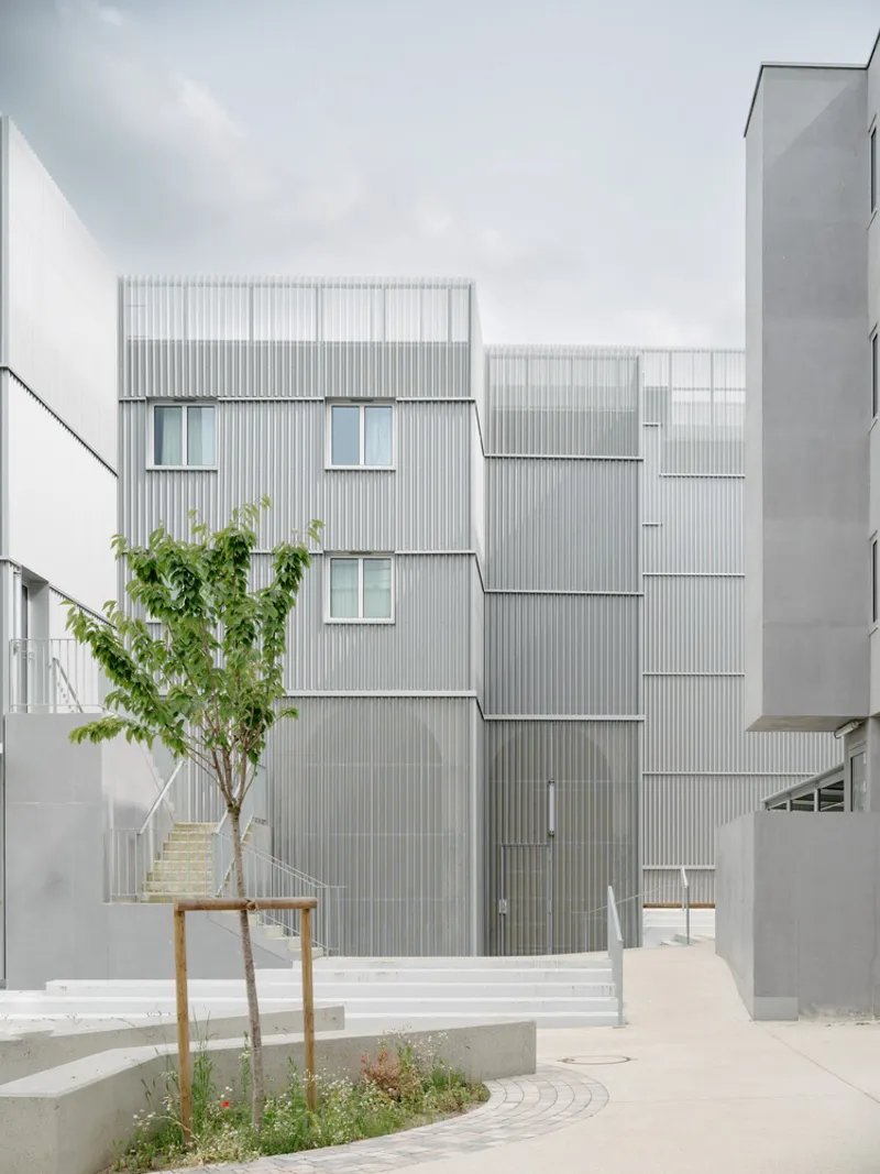 Courtyard facade showing staggered corrugated metal volumes with a young tree in a circular planter