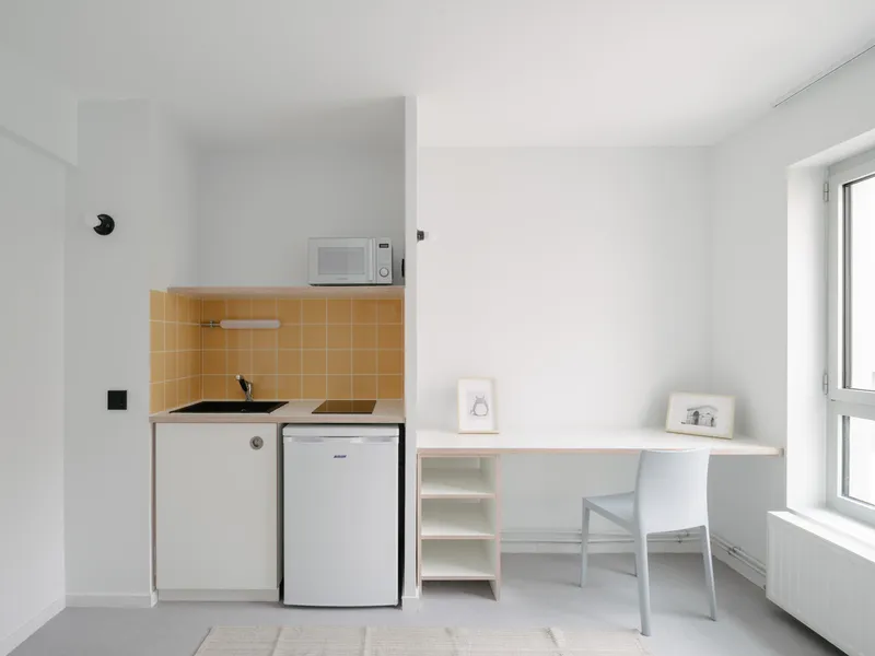 Compact kitchenette with ochre tile backsplash and white desk unit beside a window