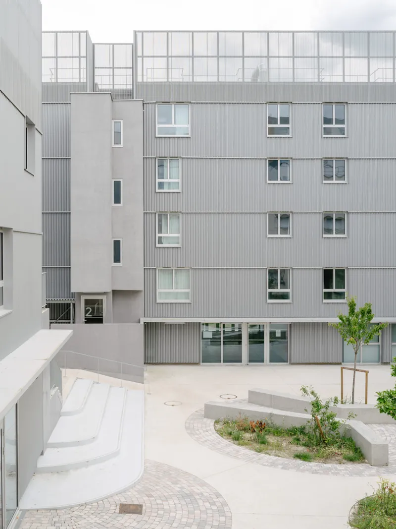Courtyard view showing corrugated metal facades with glazed balconies and planted beds under overcast sky