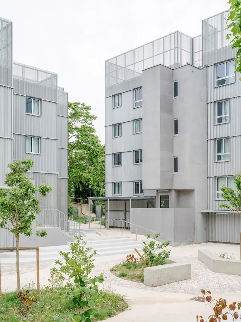 Shared courtyard with young trees and paving surrounded by grey corrugated metal and concrete residential blocks